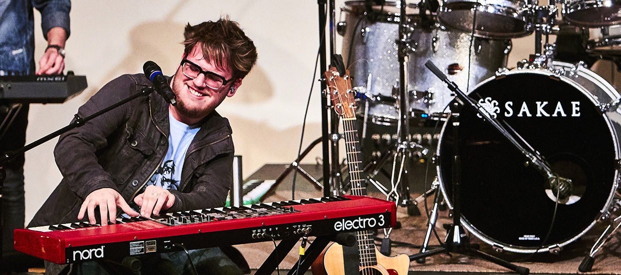 Group performs live on stage featuring man with keyboard front and center