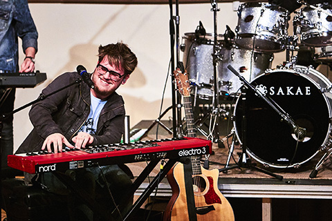 Group performs live on stage featuring man with keyboard front and center